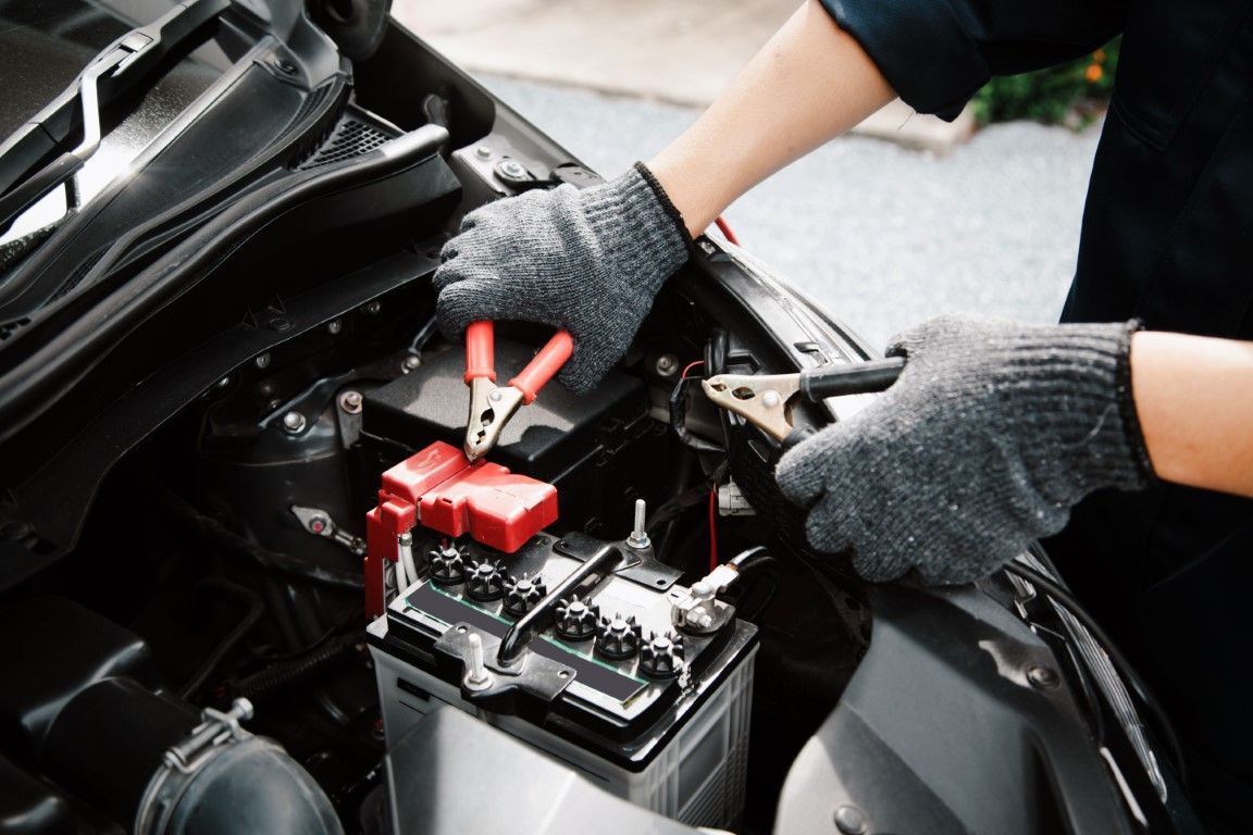 Mechanic wearing gloves jump-starting a car battery with red and black jumper cables
