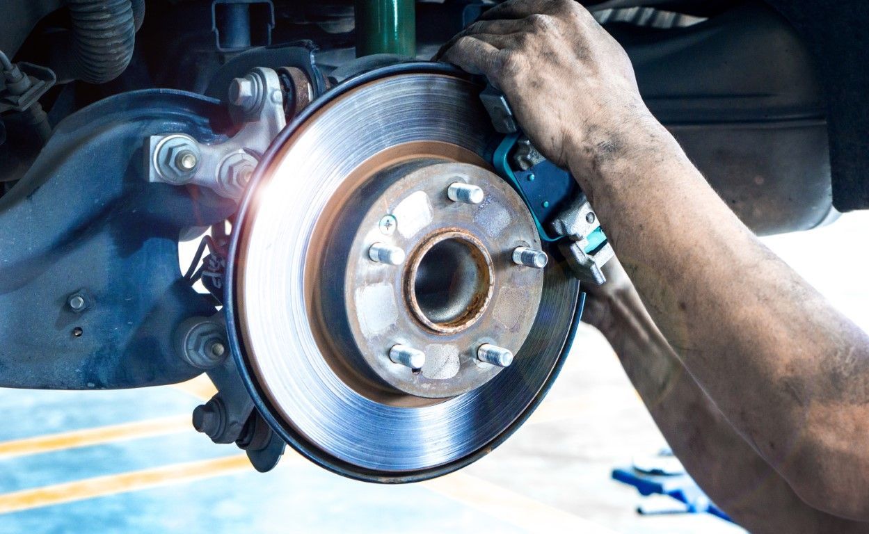 Car wheel brake rotor being serviced by a mechanic under a lifted vehicle