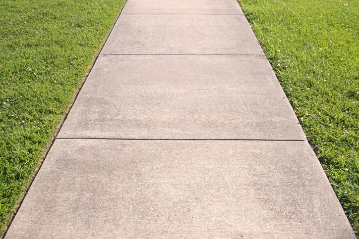 A concrete walkway going through a grassy field.