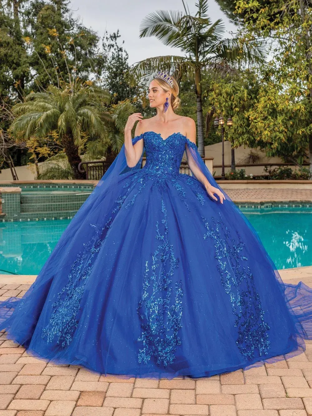 A woman in a blue ball gown is standing next to a pool.