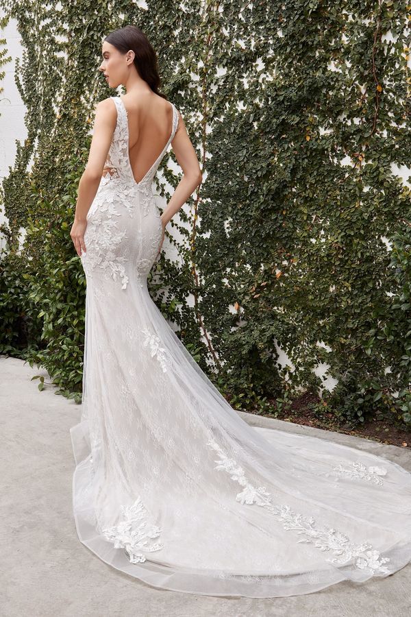 A woman in a white wedding dress is standing in front of a hedge.