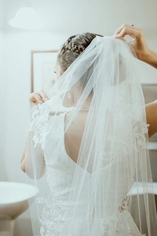 A woman in a wedding dress is putting on a veil.