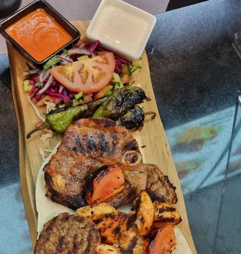 Pollo e verdure grigliate su un tagliere di legno con due salse e insalata.