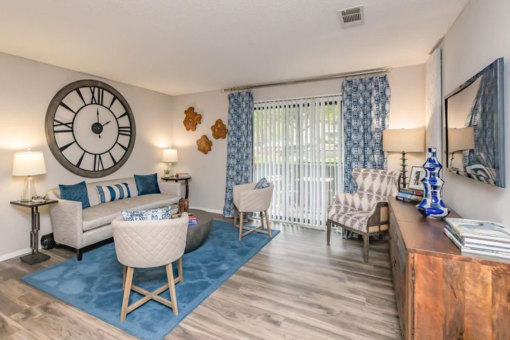 Living room with blue and tan decor, large clock, sofa, chairs, and sliding glass door.