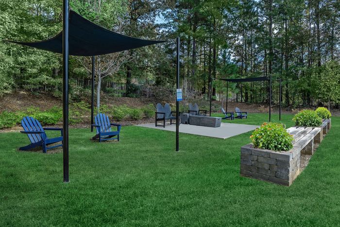 Grassy outdoor area with Adirondack chairs, fire pit, shade sails, and planters.