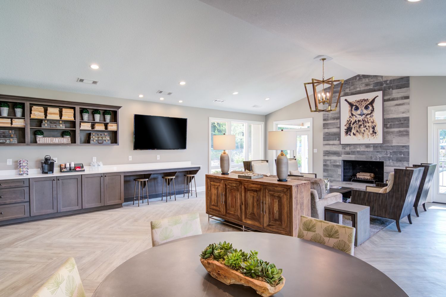 Modern lounge with fireplace, built-in bar, TV, and round table, neutral colors.
