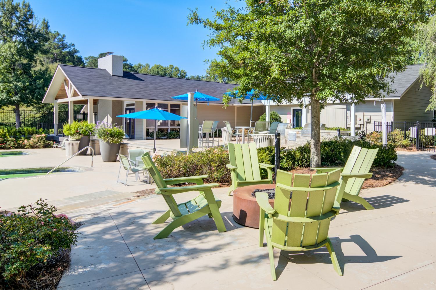 Outdoor patio with green chairs around a fire pit. Building and trees in the background on a sunny day.