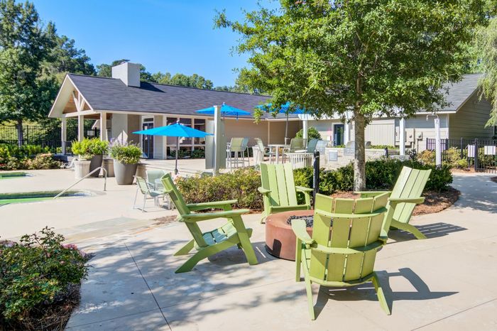 Outdoor patio with green chairs around a fire pit. Building and trees in the background on a sunny day.