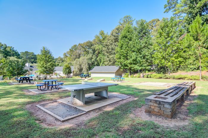 Picnic area with tables, benches, and grill set in a grassy park with trees and blue sky.