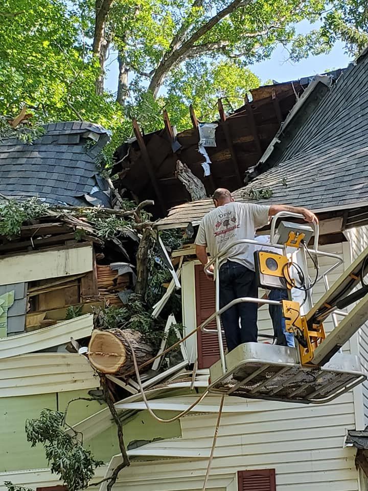 A man is working on the roof of a house that has been damaged by a tree.