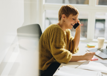 A woman is sitting at a desk talking on a cell phone.