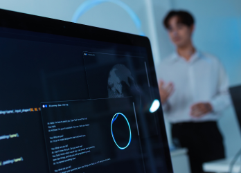 Hands typing on a laptop showing a dark code editor on a bed or cushioned surface.
