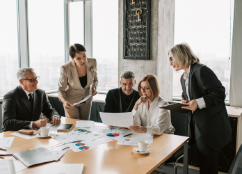 Business team meeting around a table, reviewing documents and charts in an office setting.