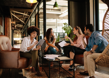 Group in a modern lounge discussing over coffee around a small table with papers and a laptop