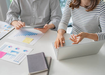 Two coworkers reviewing charts and using a laptop at a white office desk