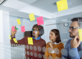 Team brainstorming with colorful sticky notes on a glass wall in a bright office.