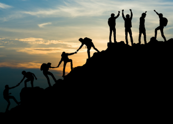 Silhouetted hikers helping each other climb a mountain at sunset