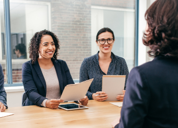 Two people smiling and taking notes during a meeting across a wooden table