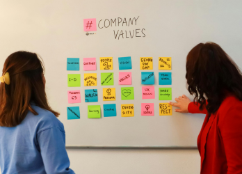 Two people viewing a whiteboard of colorful sticky notes labeled “Company Values”