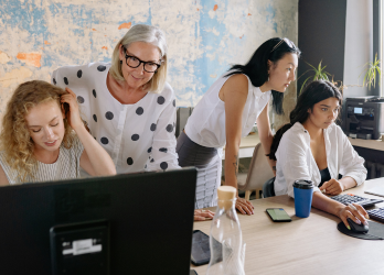 Four women looking at a computer screen in an office. One is using the mouse, others are leaning in.