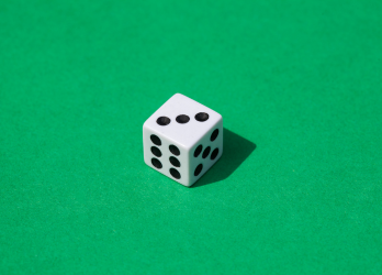 A white dice with black dots on a green surface.