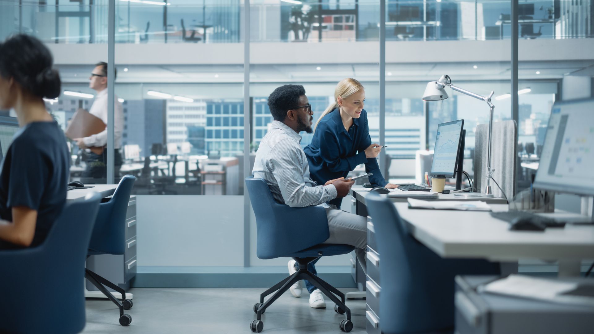 A group of people are sitting at desks in an office working on computers.