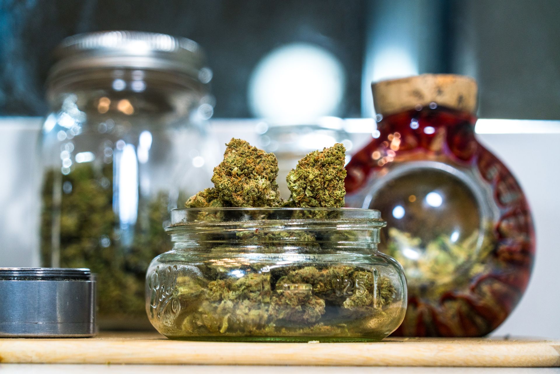 Cannabis buds in glass jars, with a grinder, on a wooden surface