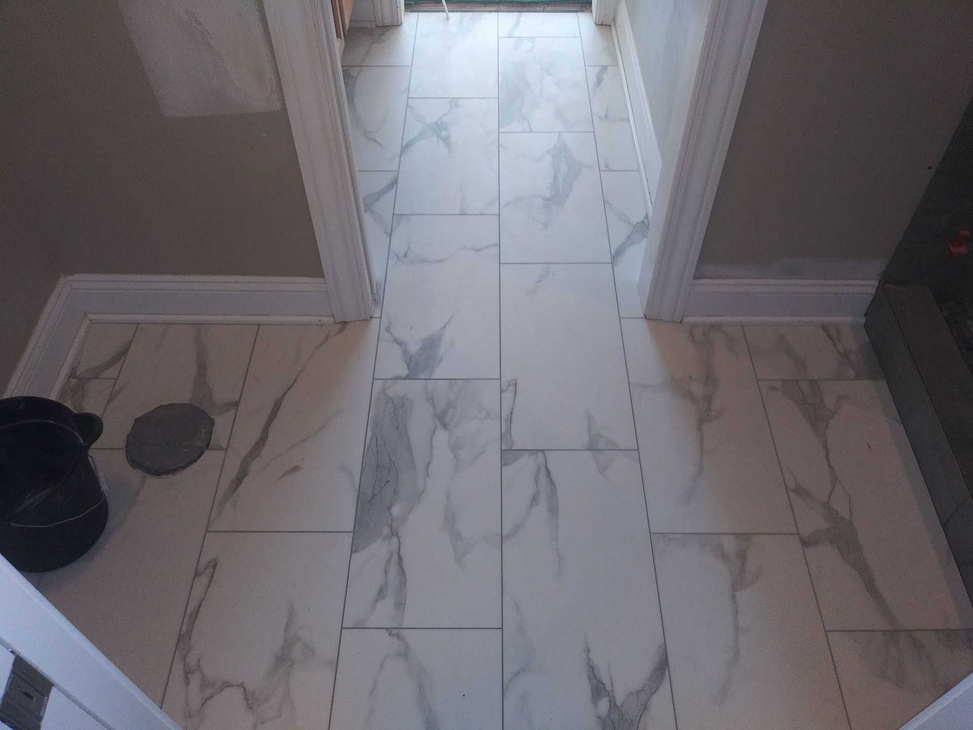 Marble-tiled hallway with a doorway, gray walls, and a black shoe on the left