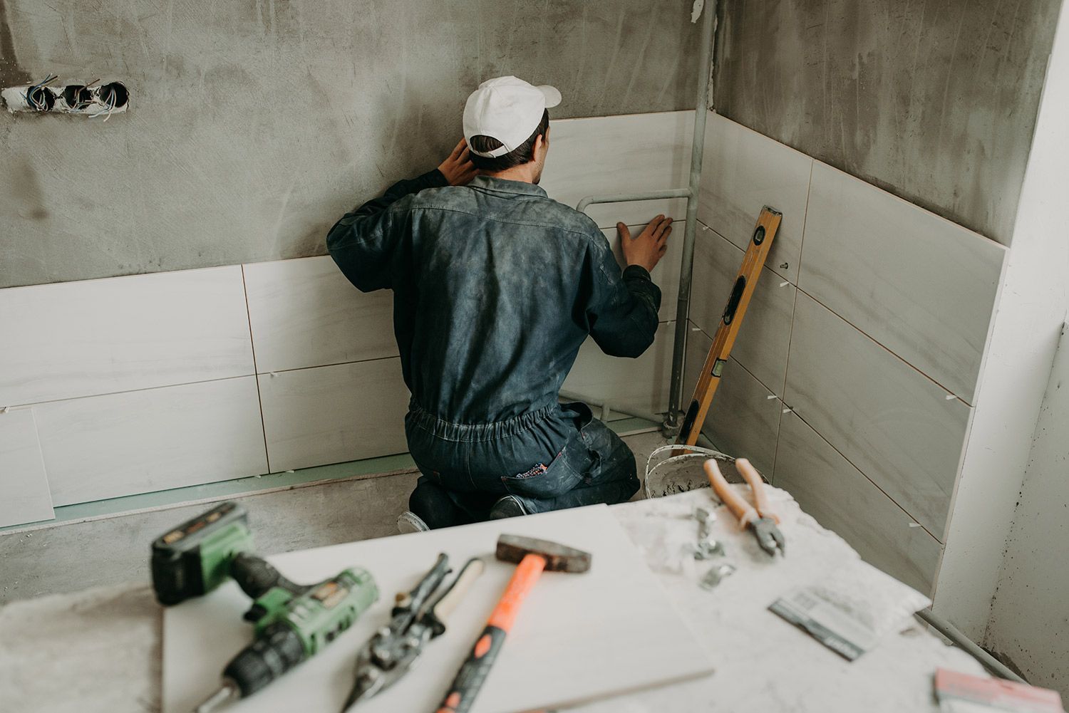 Contractor installing ceramic wall tiles in a bathroom with tools spread on a work surface.