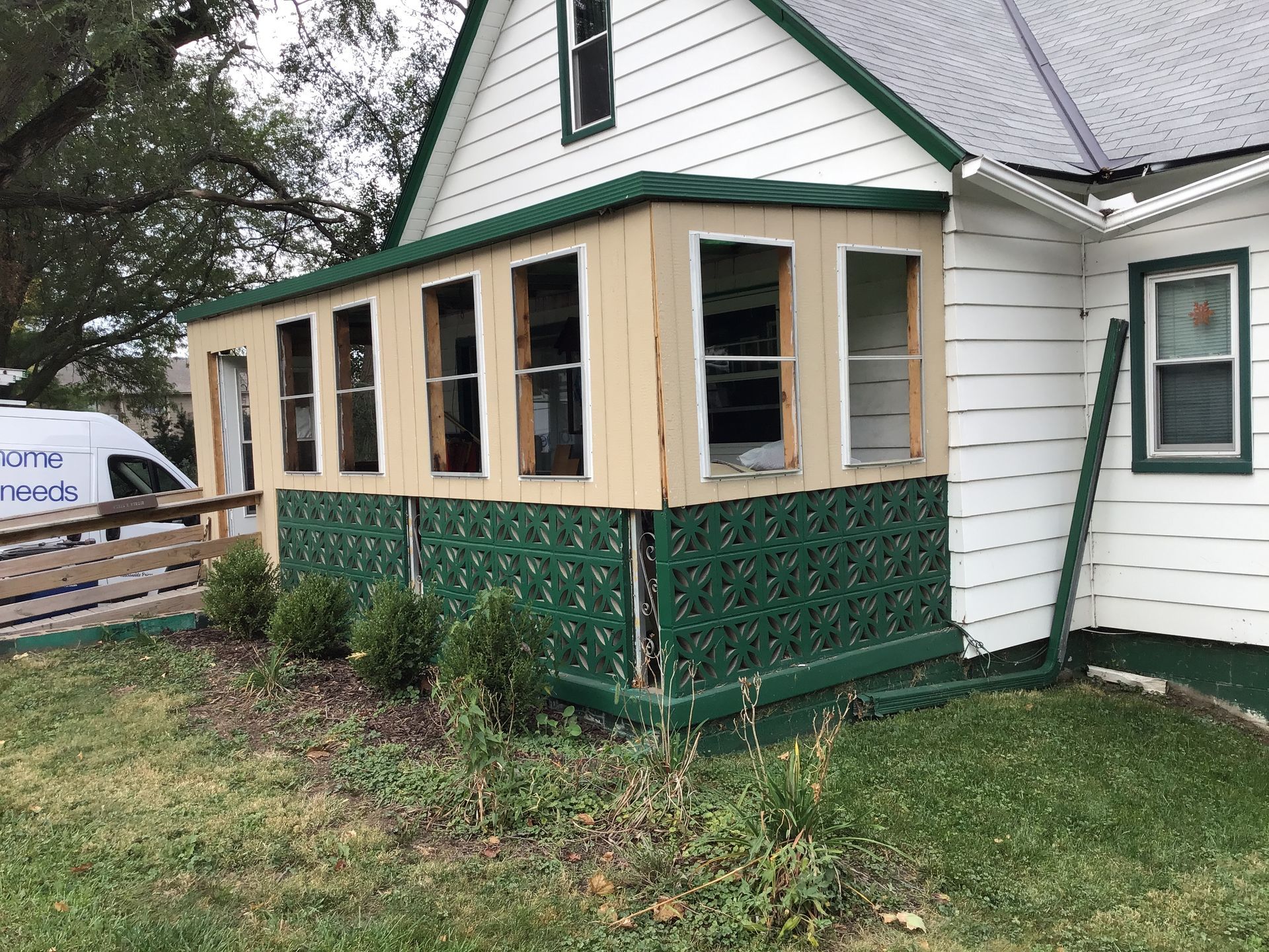 Partially enclosed porch addition with white siding, tan framing, and green lattice skirting on a house