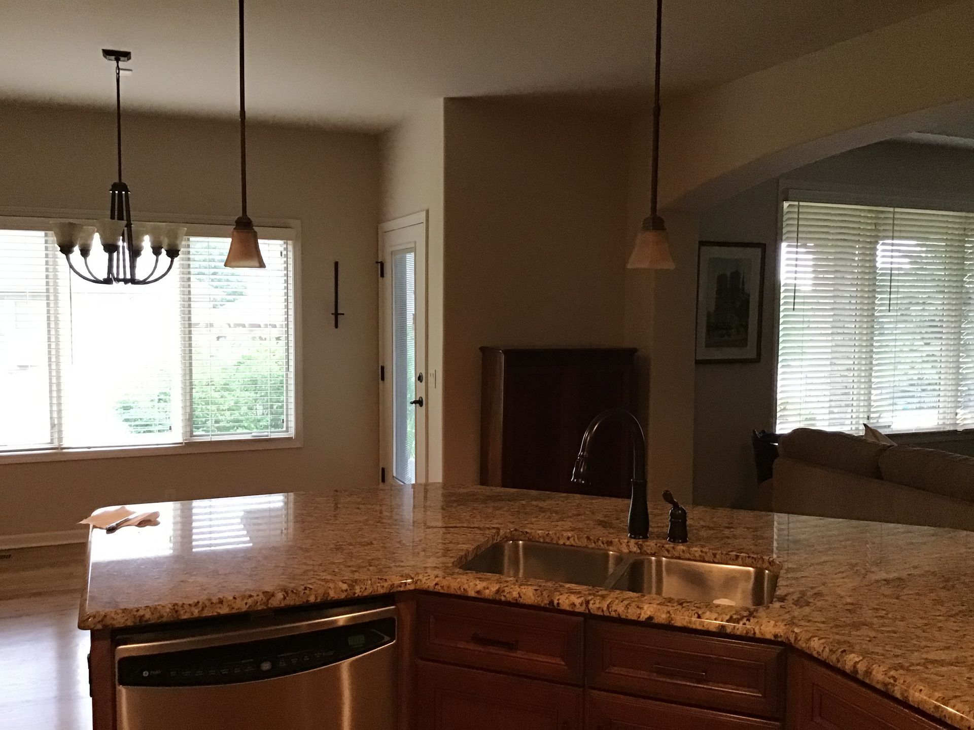 Kitchen with granite island, pendant lights, sink, and large windows overlooking a bright room
