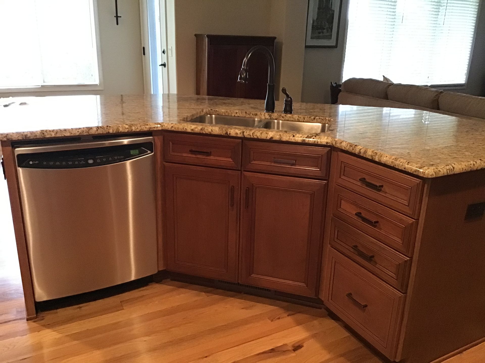 Kitchen corner with stainless dishwasher, wooden cabinets, granite countertops, and hardwood floor.