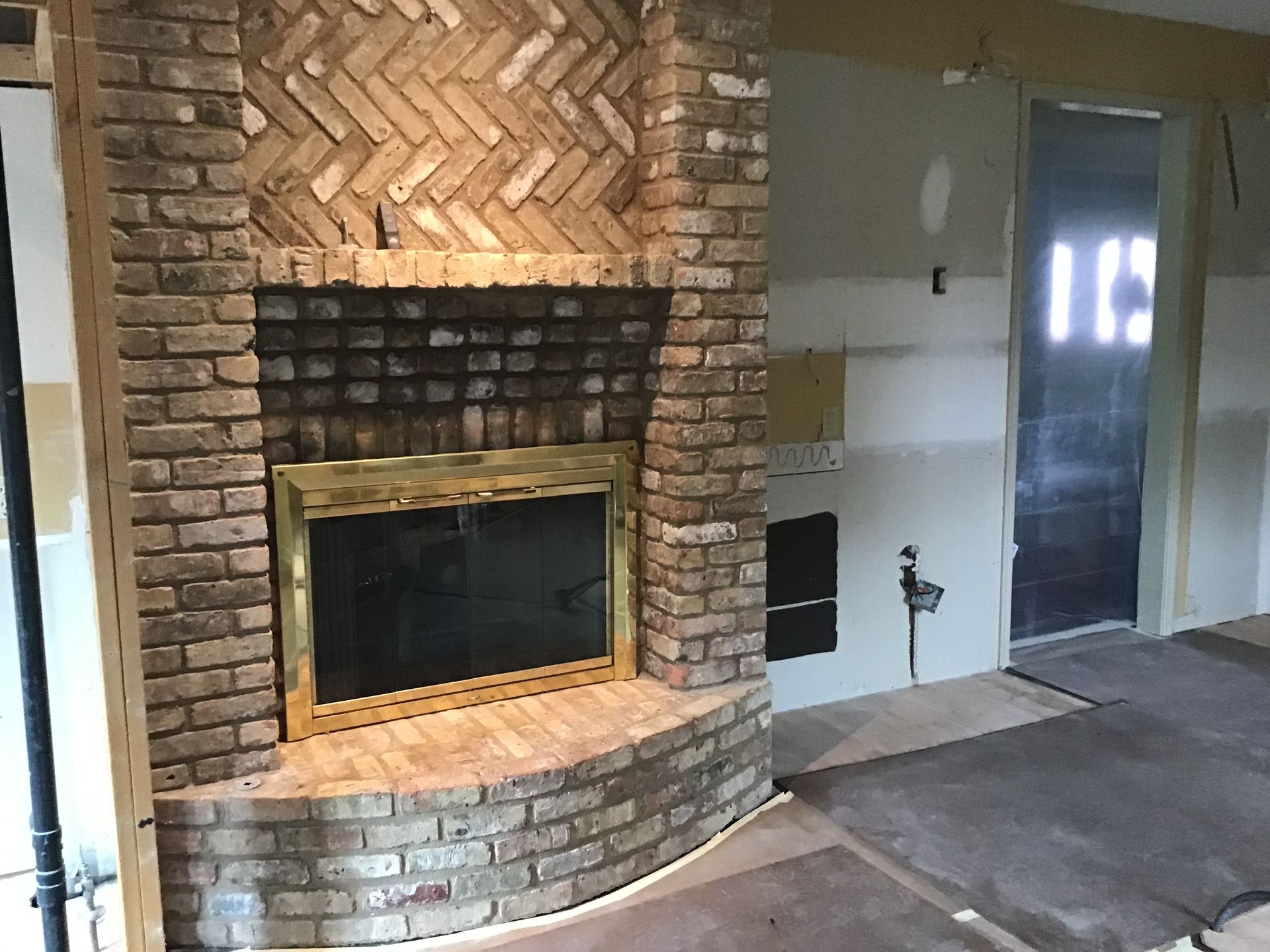 Curved brick fireplace with herringbone brick surround in a room under renovation
