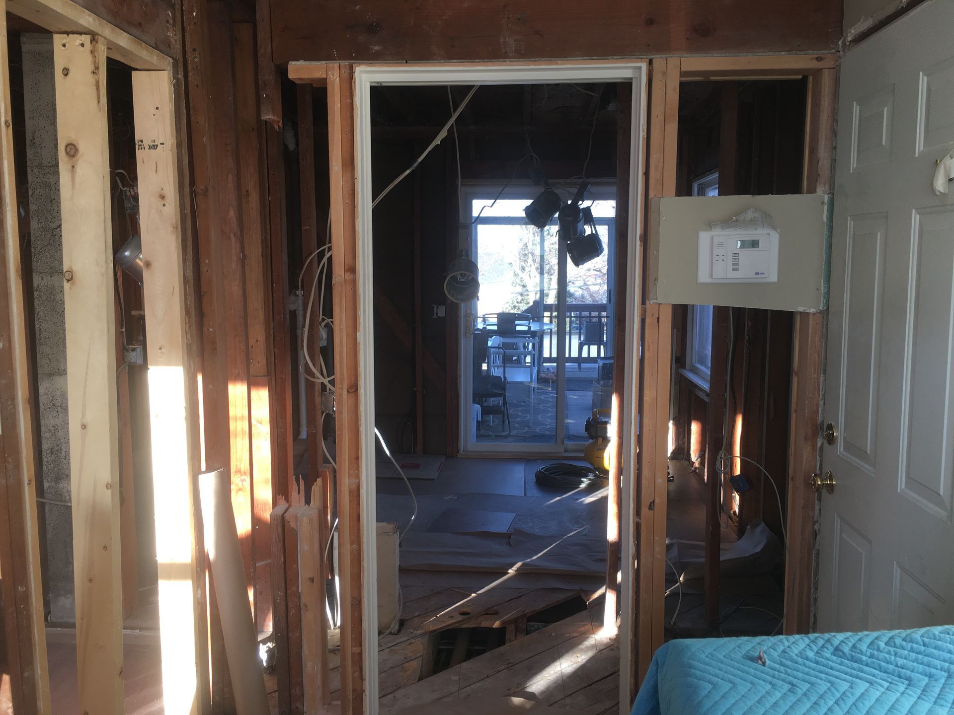 Damaged hallway with exposed studs, broken walls, and sunlight through a doorway into a cluttered room