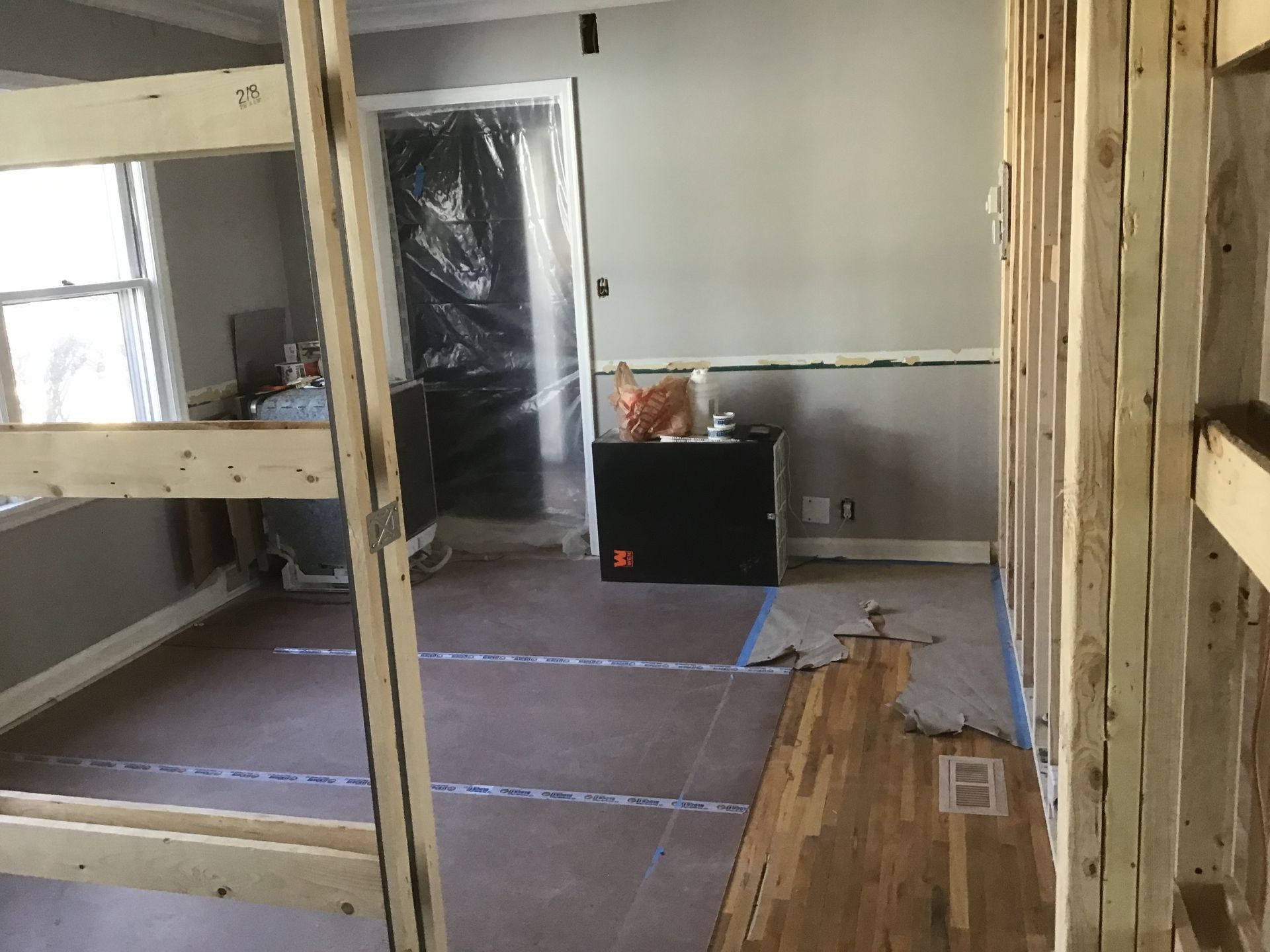Partially renovated room with exposed framing, plastic-covered doorway, and flooring under construction