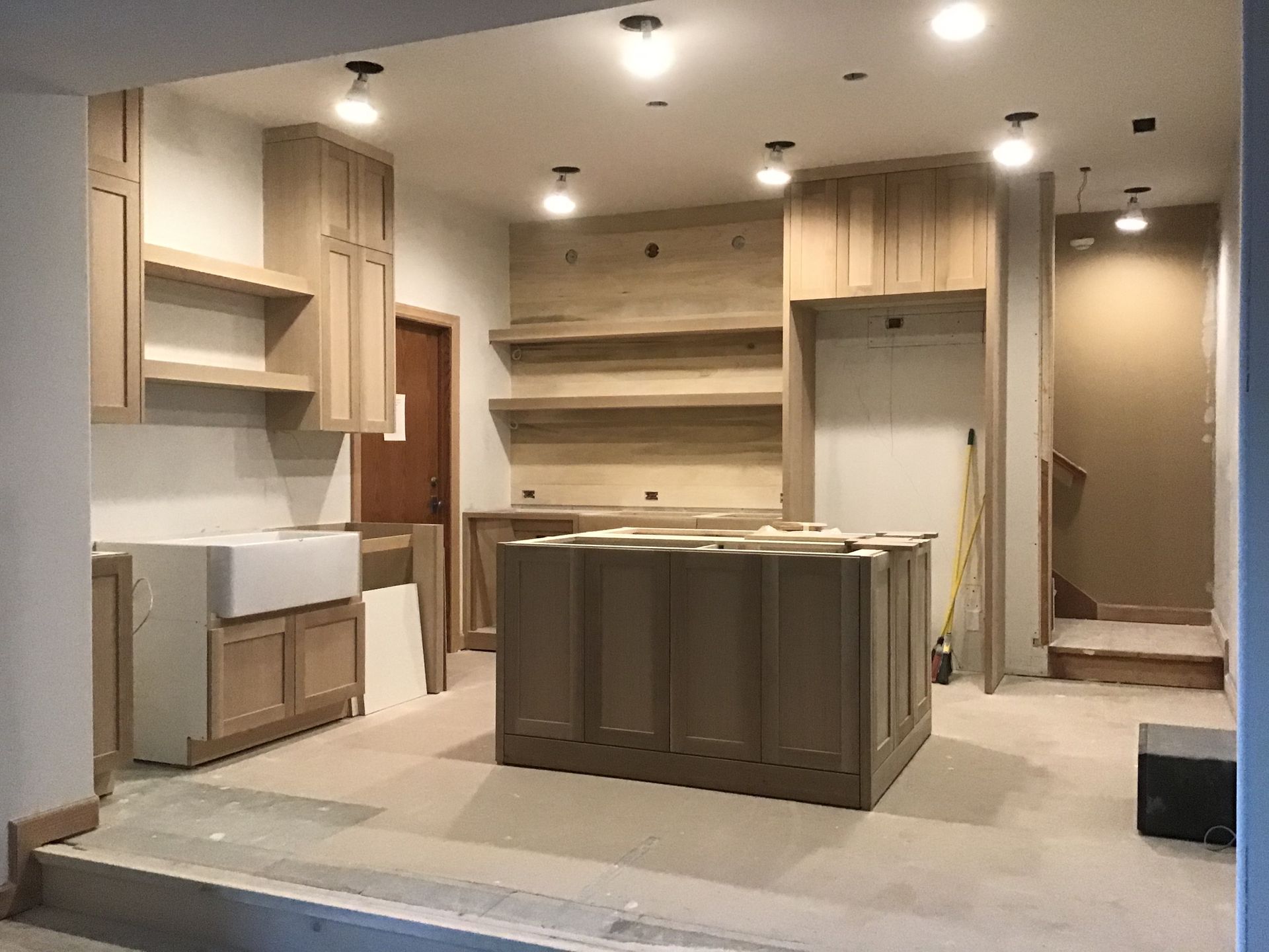 Empty modern kitchen under renovation with beige cabinets, island, and built-in shelving
