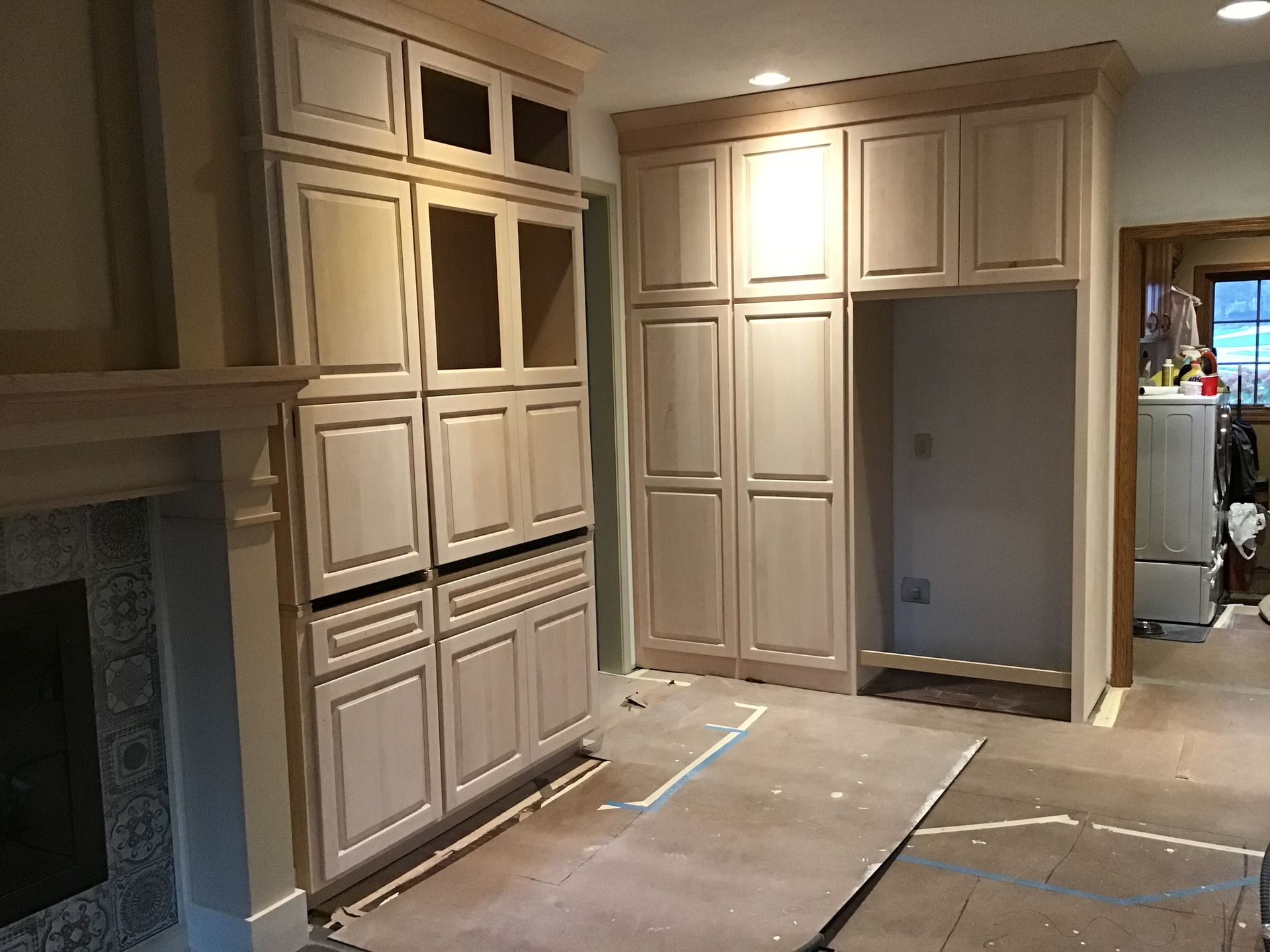 Built-in cream cabinetry and unfinished kitchen floor under renovation, with a fireplace on the left.