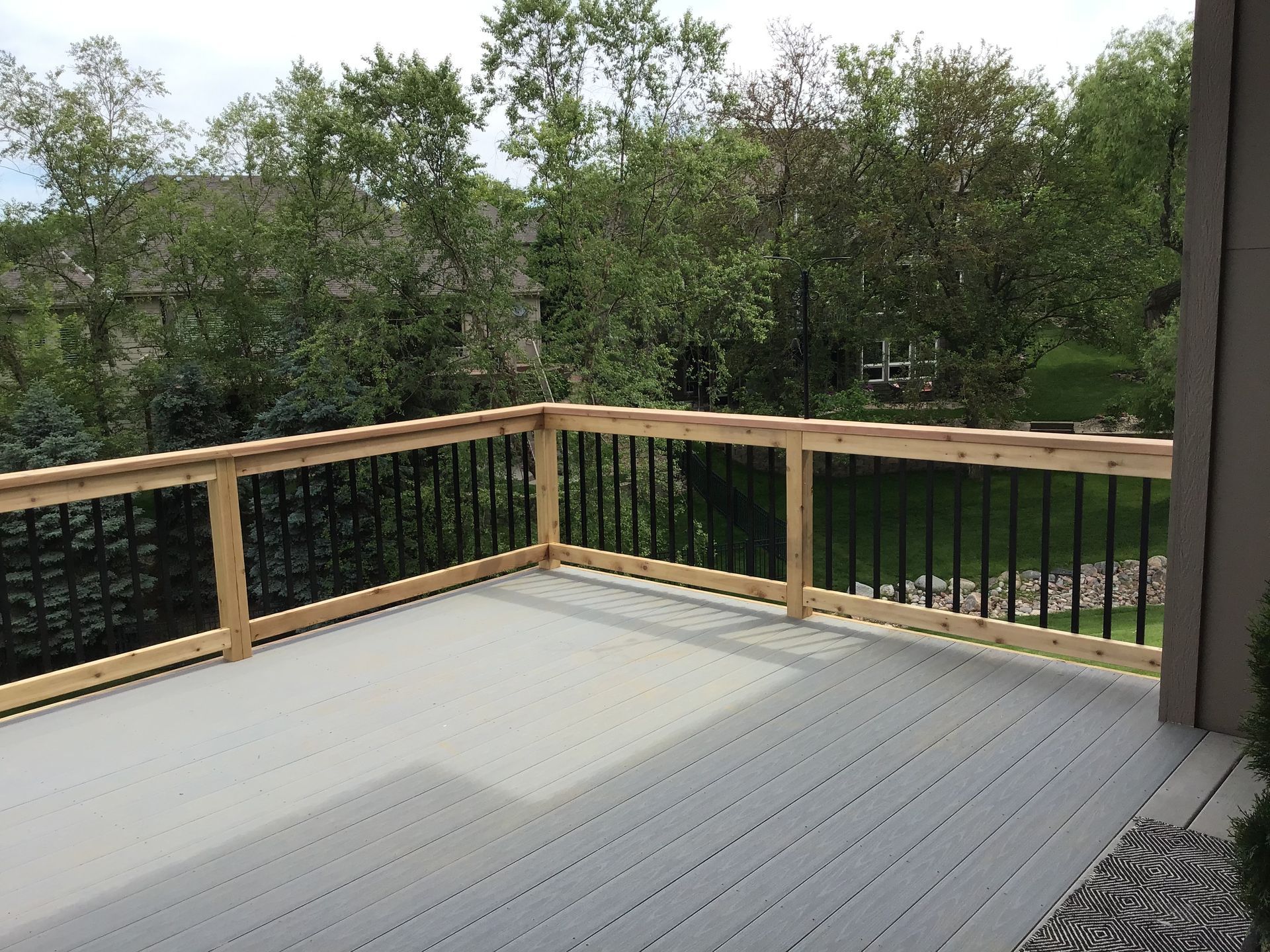 Wooden deck with black railing overlooking a green wooded landscape