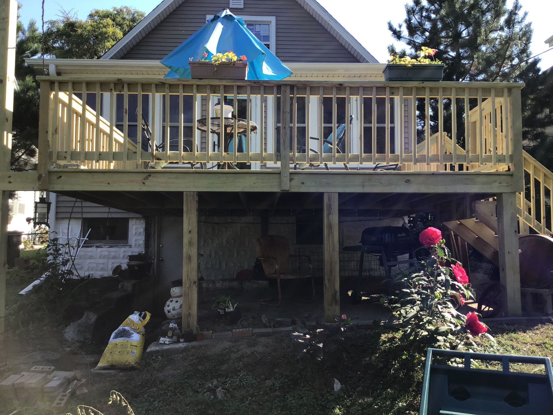 Backyard deck with blue umbrella, railing, and plants in front of a house