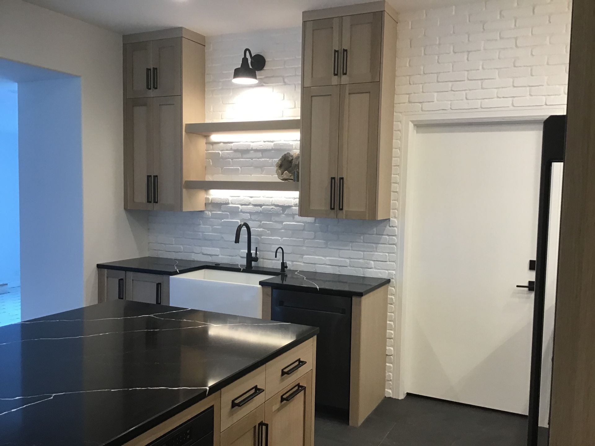 Modern kitchen with black island, white tile backsplash, wood cabinets, and a closed white door
