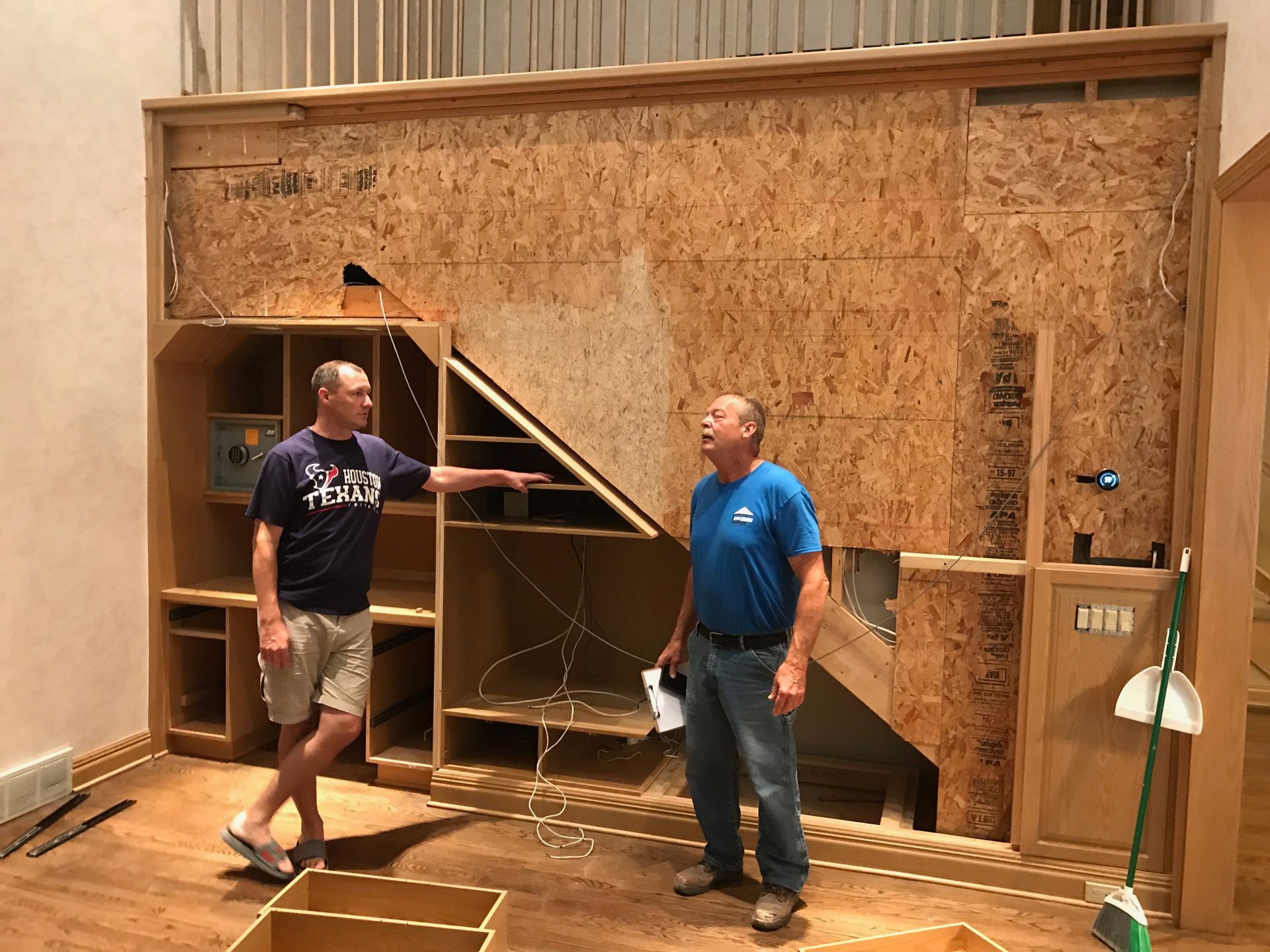 Two men standing beside a large unfinished wooden wall structure indoors