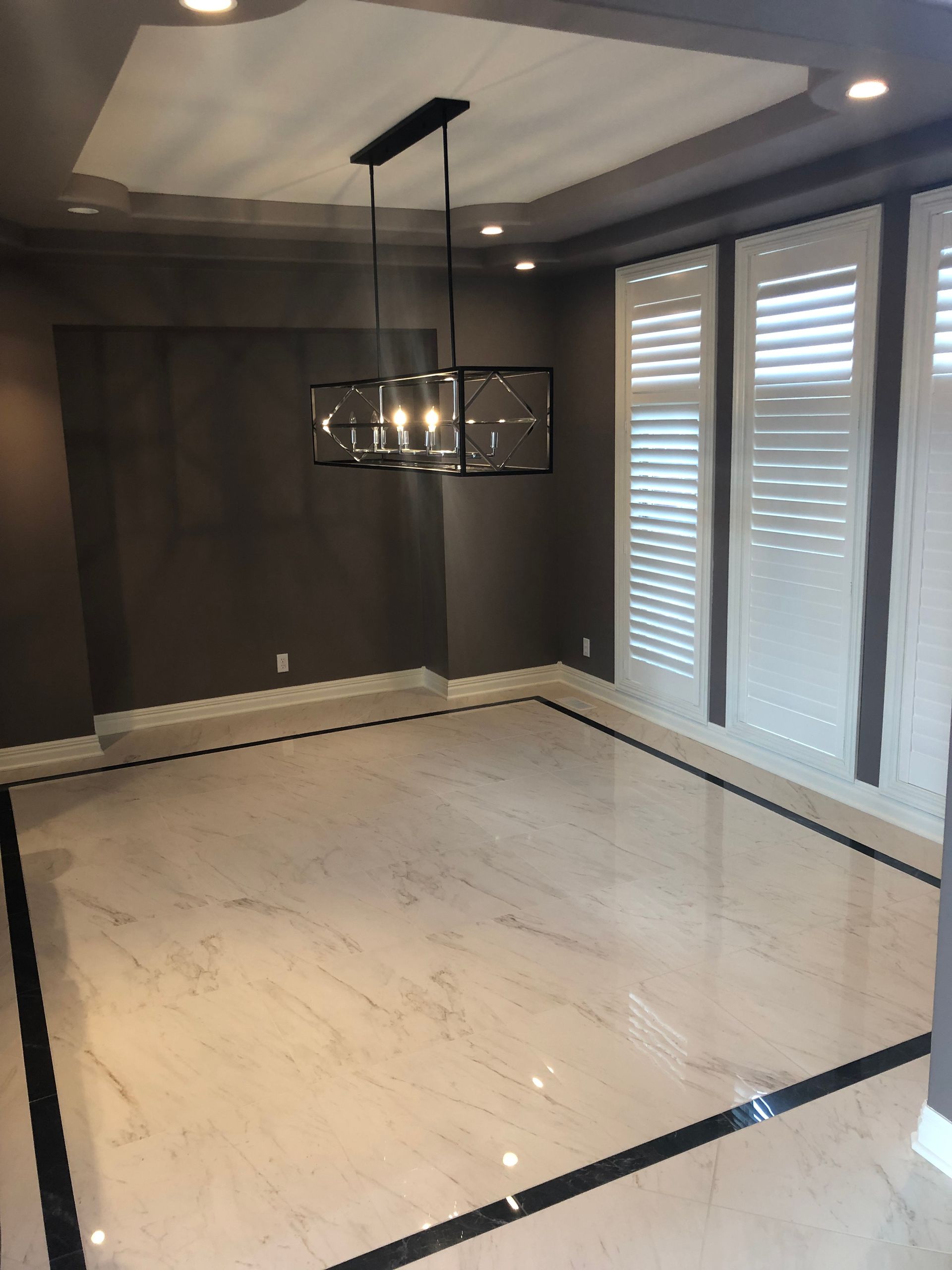 Empty modern dining room with marble floor, dark walls, pendant light, and tall windows with shutters