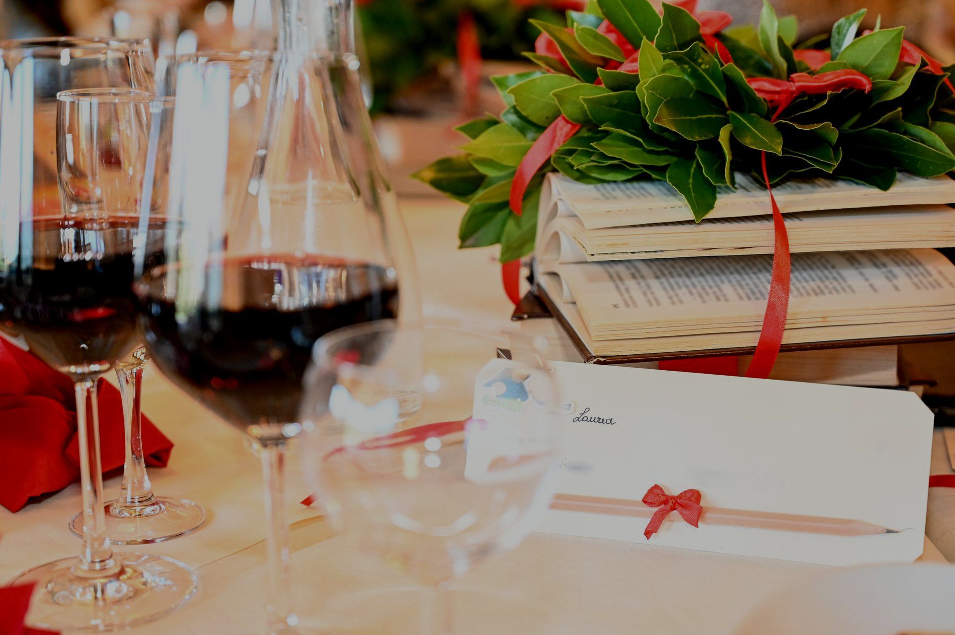 Un tavolo con due bicchieri di vino, una corona di foglie d'alloro e una pila di libri.