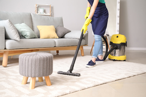 A woman is using a vacuum cleaner to clean a rug in a living room.