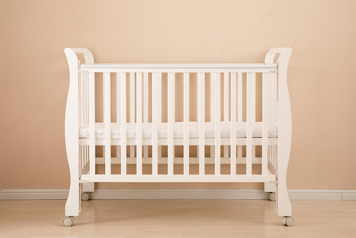 A white baby crib is sitting in front of a beige wall.
