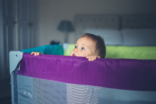 A baby is peeking over the fence of a crib.