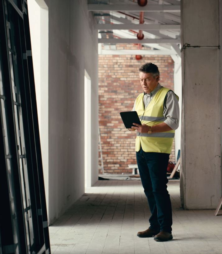A man in a yellow vest is using a tablet in a hallway.