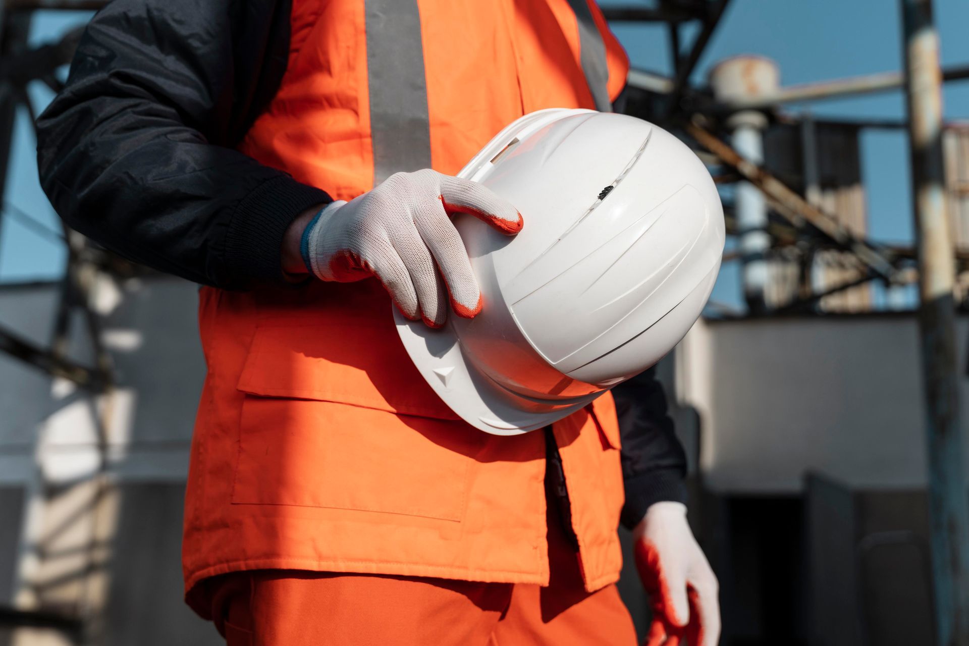 A man in an orange vest is holding a white hard hat.