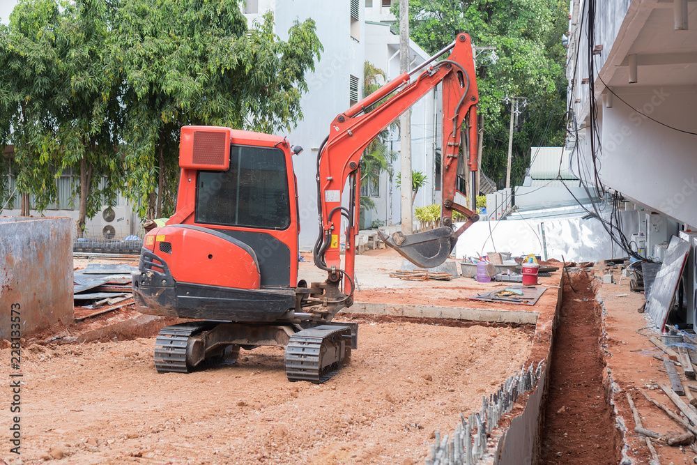 Une petite excavatrice orange travaille sur un chantier de construction.