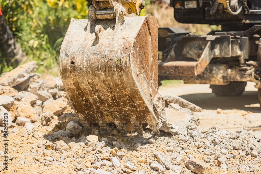 Un godet métallique d'excavatrice creuse dans un tas de terre et de roches sur un chantier de construction.
